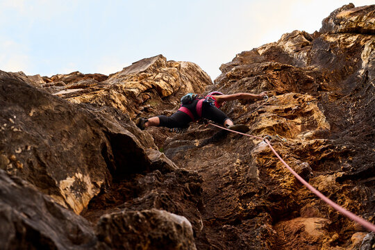 Senior Woman Climbing On Rocky Cliff Against Sky