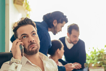 Annoyed man talking on smartphone near coworkers