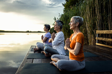 Group of senior woman doing yoga exercises by the lake.