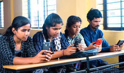 Group of teenager students busy using mobile phone while sitting on classroom - concept of technology, social media addiction and friendship.