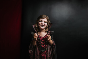 Cheerful little kid with black lips and vampire costume during carnival
