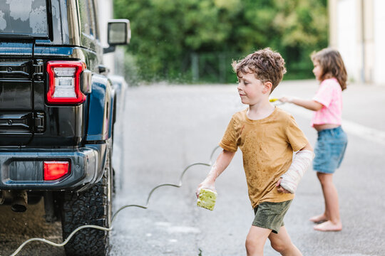 Brother Holding Sponge Washing Car With Sister In Background Outdoors