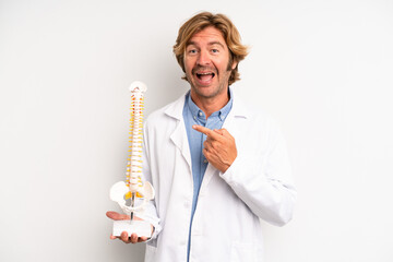 blond adult man looking excited and surprised pointing to the side. physician or doctor concept