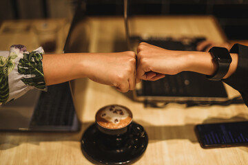 Two hands fistbump together with laptop and coffee in the background. Friendship, teamwork, respect, commitment, deal concept and symbol.