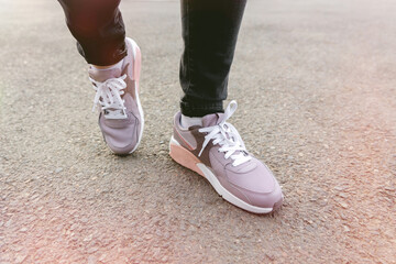 Fototapeta na wymiar cropped image of female legs in shoes. Woman in black jeans and pink sneakers stands on pavement