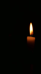 Vertical image of glowing candle and flame against black background