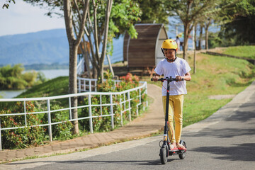 Portrait of  little Asian boy wear helmet enjoy having fun riding electric scooter at street park outdoors on sunny day. Healthy sport children activities outside. © Gatot