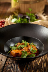 Traditional georgian food - chicken chakhokhbili in black plate on wooden background. Georgian chicken stew with herbs on wooden table. Chakhokhbili with tomatoes and herbs in rustic style.