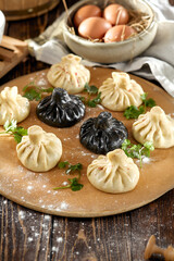 Composition of georgian khinkali on wooden table with coriander leaves. Georgian food - classic and black khinkali in rustic style. Traditional georgian dumplings khinkali on wooden background.
