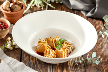 Traditional russian dessert - honey cake with berry sauce on wooden background. Sliced Honey cake in white plate on wooden table. Layered cake medovik in rustic style.