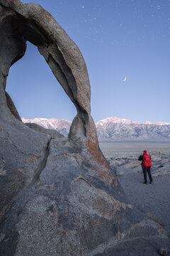 Anonymous traveler near rocky formations in wild nature in starry sky