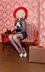 Curly girl - blonde in a blouse with polka dots - pin-up, with a suitcase calls on an old telephone in a red room. Retro style