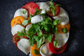 Fresh homemade caprese salad on a slate black plate. Mozzarella, basil and three kinds of tomatoes. Italian cuisine. Appetizer. Top view. Flat lay.