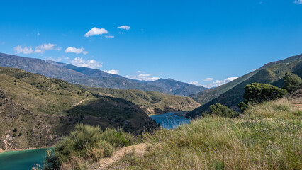 Breath-taking view from the top on green lake surrounded by picturesque mountain alley with trees and bushes in sunny summer day with blue sky and white clouds in background.