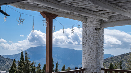 Fototapeta na wymiar Spectacular view to the mountain valley in summer day from open terrace of white building with white wooden roof and decorative lights fixed to the roof with blue sky and white clouds in background