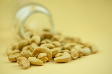 Cashew nuts in an open glass jar are scattered. Minimalist food photography style
