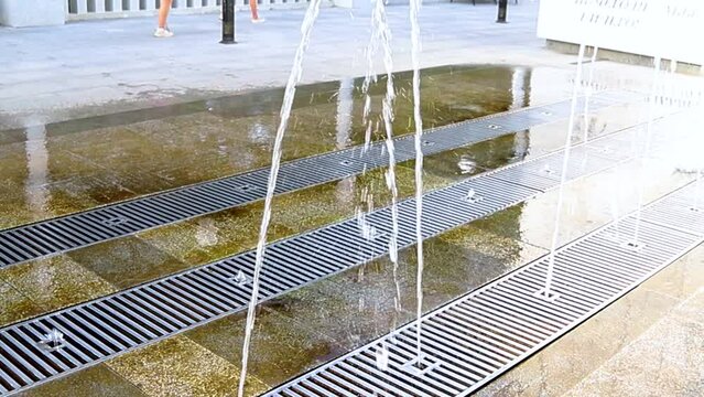 Fountain in the city park. A jet of water escapes from under the grate to the ground. Children's entertainment in the park. Cool water on a hot day.