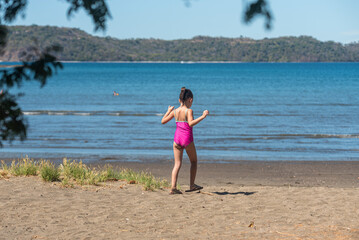 Horizontal image of an unrecognizable little latina girl walking straight towards the shore of the beach. 