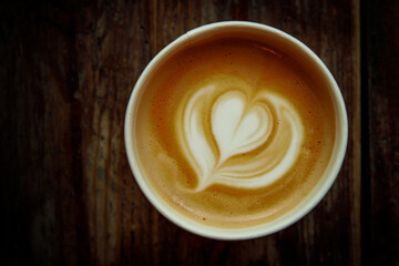 A cup of cappuccino with a heart latte art. Vintage wooden background, top view.