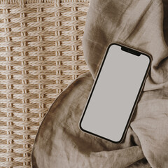 Flatlay mobile phone, neutral beige muslin linen cloth on rattan bench. Aesthetic elegant blog,...