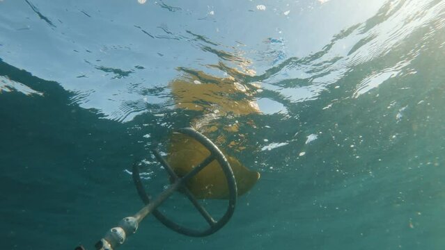 Scuba divers view ascending from below the water next to a dive flag bobbing on the ocean surface.