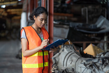 Woman worker working at old automotive spare parts warehouse. Woman warehouse worker checking old engine, motor, machine at the garage industry factory.