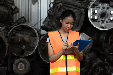 Woman worker working at old automotive spare parts warehouse. Woman warehouse worker checking old engine, motor, machine at the garage industry factory.
