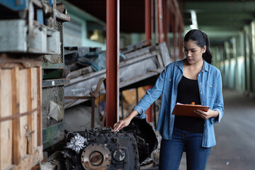 Asian woman worker working at old automotive spare parts warehouse. Woman warehouse worker checking old engine, motor, machine at the garage industry factory.