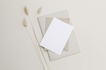 Modern summer stationery still life. Lagurus ovatus, bunny tail grassy foliage. Blank paper greeting card and diary mock up scene, craft envelope. Beige table background. Neutral flat lay, top view.