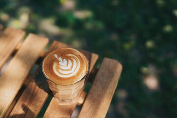 A glass of hot coffee latte on wooden table with copy space and beautiful warm light.