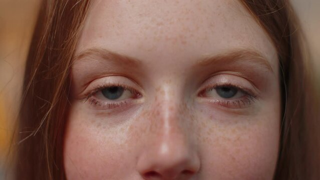 Extreme close-up macro portrait of freckles smiling girl face. Teen beautiful kid's eyes, looking at camera. Blue eyes of redhead female child model. Young positive cute children opening wide her eyes