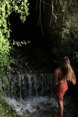 blonde young girl moves her hair in nature next to a small waterfall