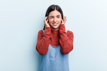 Young caucasian woman isolated on blue background covering ears with hands.