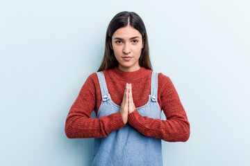 Obraz premium Young caucasian woman isolated on blue background praying, showing devotion, religious person looking for divine inspiration.