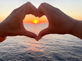 Hands making the shape of a heart with the sunset sun in the background in a beach landscape. Motivational concept.