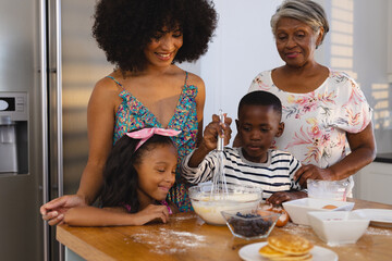 Multiracial senior woman and mid adult woman looking at children whisking batter in bowl on table