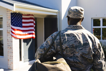 Rear view of army soldier in camouflage clothing with backpack standing outside house in yard