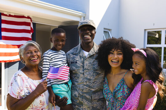 Portrait of happy multiracial army soldier in camouflage clothing with family standing in yard