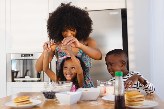 Multiracial Mother With Afro Hair Breaking Egg With Daughter In Bowl While Making Breakfast On Table