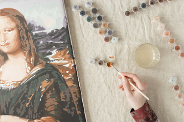 Painting by numbers with acrylic paints. Woman coloring Mona Lisa picture by numbers, hand with...