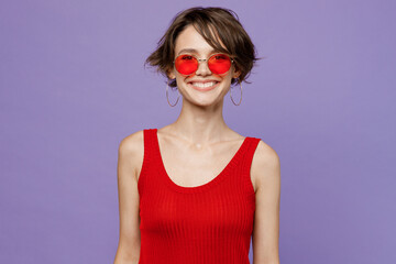 Young smiling happy cheerful fun cool caucasian european woman 20s she wearing red tank shirt eyeglasses look camera isolated on plain purple color backround studio portrait. People lifestyle concept.