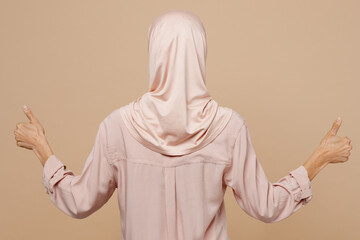 Fototapeta premium Back rear view young arabian asian muslim woman she wearing abaya hijab pink clothes show thumb up isolated on plain pastel light beige background. People uae middle eastern islam religious concept.