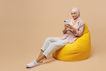 Full body young arabian asian muslim woman she wear abaya hijab pink clothes sit in bag chair hold...
