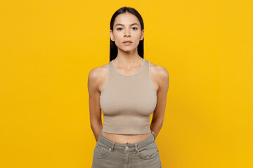 Young attractive beautiful calm serious brunet latin woman 30s she wearing basic beige tank shirt looking camera isolated on plain yellow color wall backround studio portrait People lifestyle concept