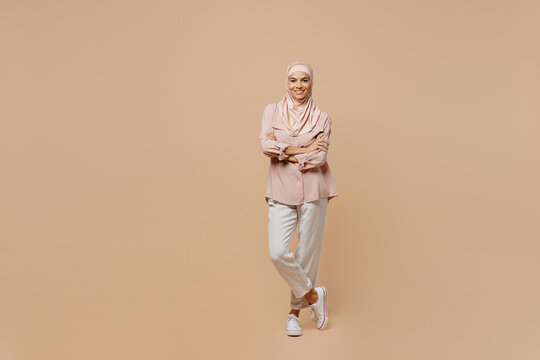 Full body young arabian asian muslim woman she in abaya hijab pink clothes hold hands crossed folded isolated on plain pastel light beige background People uae middle eastern islam religious concept