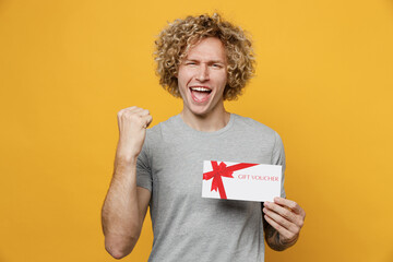 Young happy excited amazed caucasian man 20s he wear grey t-shirt look camera hold gift certificate...