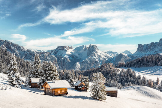 Picturesque landscape with small wooden log cabin on meadow Alpe di Siusi on sunrise time. Seiser Alm, Dolomites, Italy. Snowy hills with orange larch and Sassolungo and Langkofel mountains group