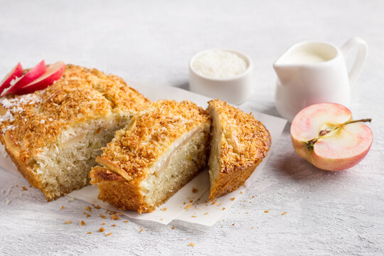 Coconut cake, mannik with apples and cream in a ceramic baking dish on a light gray textured background. Delicious homemade food