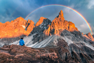Tourist in Dolomite Alps. Pale di San Martino mountain group in sunset time. Hight mountains with glacier glowing by sunset light with rainbow. San Martino di Castrozza, Dolomites, Trentino, Italy