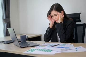 Stressed young business woman working on laptop with documents in modern office, workload concept